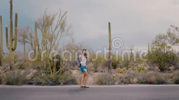 慢镜头宽镜头快乐年轻的旅游妇女拍照走在史诗般的仙人掌沙漠道路上美国国家公园视频的预览图