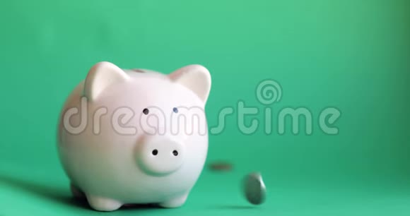 绿色背景上的硬币落在猪储蓄罐上视频的预览图