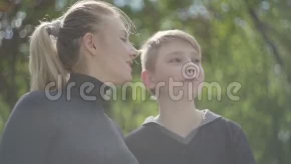 一位年轻的母亲和她十几岁的儿子一起在公园里休息那个女人亲吻她的孩子的脸颊他吻她视频的预览图