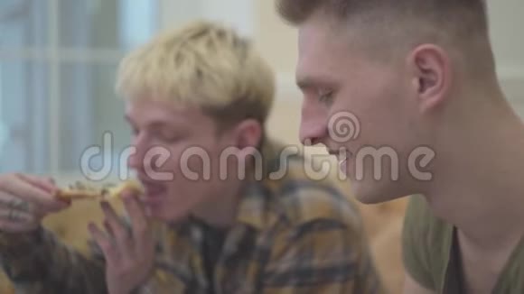 两个年轻人坐在客厅的沙发上吃着美味的食物比萨饼肉和阿鲁古拉近在咫尺休闲视频的预览图