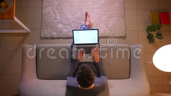 年轻商人坐在室内沙发上用绿色屏幕在笔记本电脑上工作的特写镜头视频的预览图
