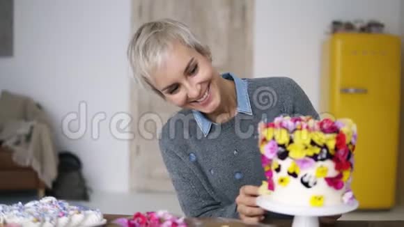 穿灰色毛衣的微笑女人在白色的现代厨房工作室里用花装饰蛋糕女厨师是一名高级厨师视频的预览图