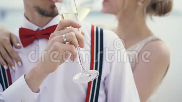 特写镜头新婚夫妇在露天喝香槟穿着吊带和红色领结的时髦年轻新郎金发新娘视频的预览图