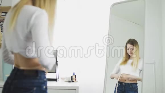 穿白色上衣的布鲁内特女孩用前镜的卷尺测量腰围视频的预览图