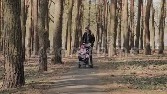 漂亮的女人和她的小女儿一起走在公园里推着婴儿车妈妈带着婴儿车走在视频的预览图