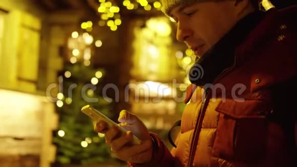 穿红色夹克的年轻人在晚上使用智能手机来抵御圣诞节的光照红色摄像机拍摄视频的预览图