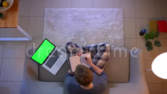 年轻商人坐在绿色屏幕上用笔记本电脑做笔记的特写镜头视频的预览图