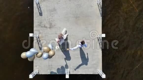 空中视频顶部景观美丽的新婚夫妇新娘和新郎在户外跳舞在码头上新郎拿着气球视频的预览图