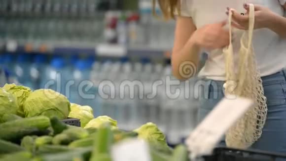 漂亮的女孩子在超市里用网状有机购物袋摘蔬菜和水果零浪费环保视频的预览图