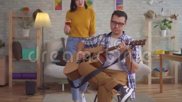 一位带着酒杯弹吉他的年轻音乐家被一位带着酒杯的年轻女子走近视频的预览图