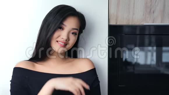 在现代厨房里一个穿着裸肩摆姿势看镜头的可爱的亚洲年轻女人视频的预览图