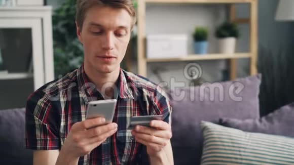 帅哥正在用信用卡在线支付触摸智能手机屏幕然后开心地坐在上面微笑视频的预览图