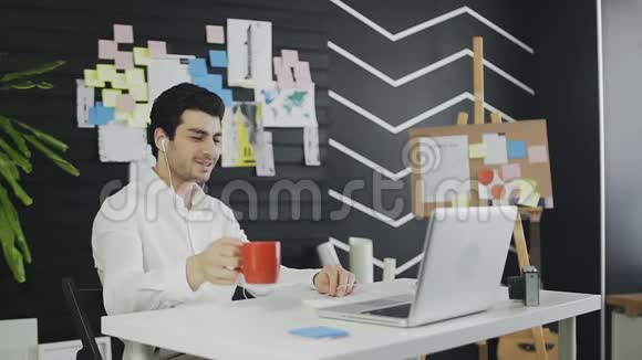 快乐的商人戴着耳机看着笔记本电脑喝着咖啡视频的预览图