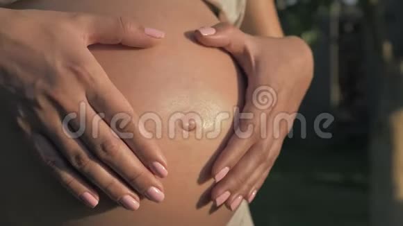 孕妇用双手在夕阳下把心放在肚子上视频的预览图