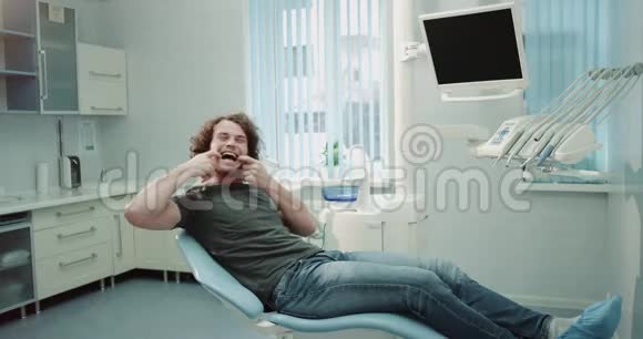 坐在牙医椅上的一个年轻的快乐病人微笑着直视着摄像机视频的预览图