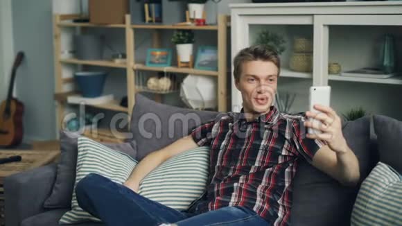 快乐的年轻人用智能手机做在线视频通话谈笑风生地看着坐在沙发上的屏幕视频的预览图
