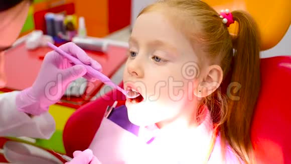 孩子们牙医在一张黄红色的牙椅上检查一个可爱的红发小女孩的牙齿和嘴视频的预览图