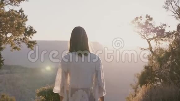 电影背光拍摄的年轻快乐的女人穿着白色的衣服享受惊人的大峡谷全景日落视频的预览图