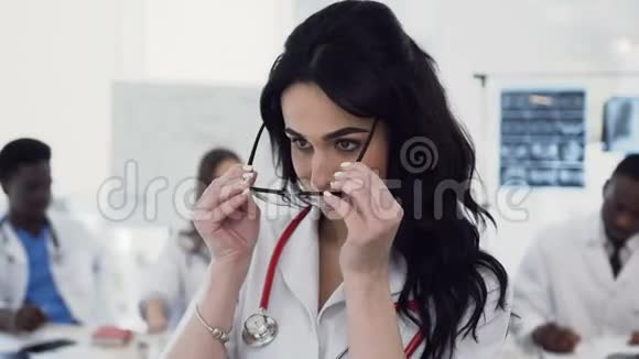 一位戴眼镜的年轻漂亮女医生的画像正看着镜头她的同事们正在微笑视频的预览图