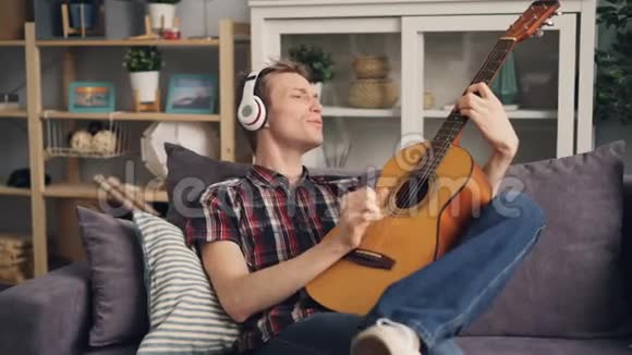 有创造力的年轻人正在弹吉他唱最喜欢的歌用耳机听音乐在现代放松视频的预览图