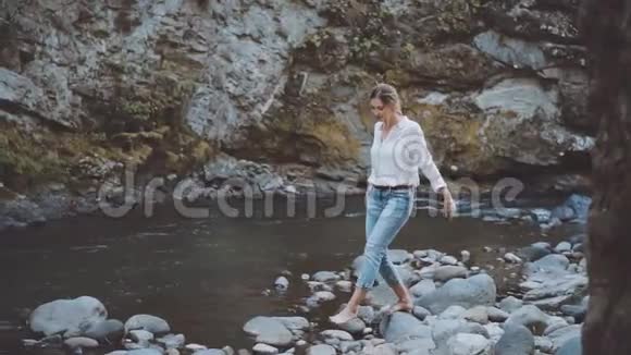 美丽苗条的金发女郎光着脚走在干净的博尔若米河附近的岩石上穿着白色波尔卡多特的女士视频的预览图