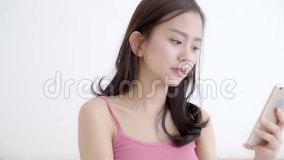 美丽的肖像年轻的亚洲女人微笑着坐着看着智能手机阅读社交网络与享受床视频的预览图