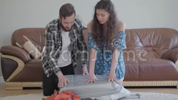 男人和女人坐在家里的地板上在皮革沙发前在旅行前收拾一个手提箱也有一些视频的预览图
