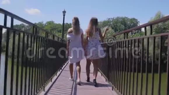 两个年轻的女人在公园的小桥上散步视频的预览图