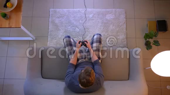 年轻的穿着随意的男性用游戏机坐在沙发上玩电子游戏电视的特写镜头视频的预览图