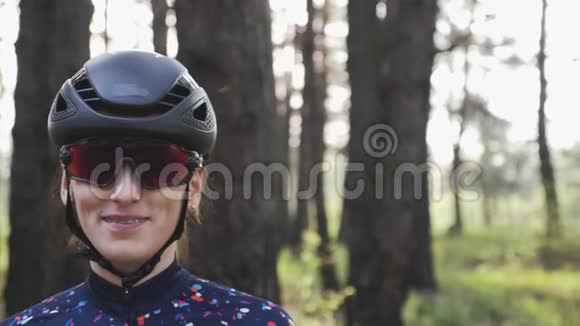 年轻迷人的骑自行车女人戴着黑色头盔和眼镜微笑着的肖像自行车概念慢动作视频的预览图