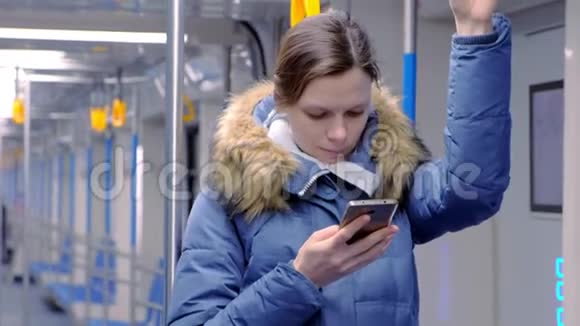 疲惫的女人坐在空的地铁车上浏览她的智能手机的肖像站立并握住扶手视频的预览图