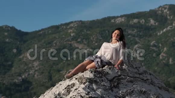 阳光明媚的一天美丽的年轻女子模特坐在岩石上慢动作视频的预览图