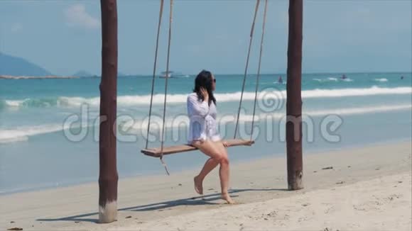 年轻美丽的快乐女人在海滩上享受着大海背景下的秋千视频的预览图