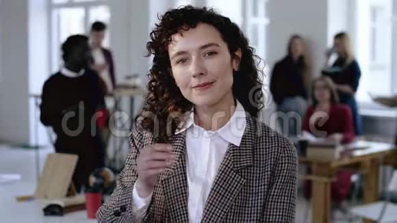 年轻严肃的欧洲商务女性穿着正式西装摸着她的深色卷发摆着现代办公背景视频的预览图