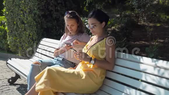 两个年轻女孩坐在长凳上只看着一部手机视频的预览图