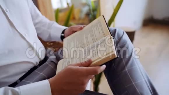 一个穿着白色衬衫坐在扶手椅上的无名男子正在看书视频的预览图