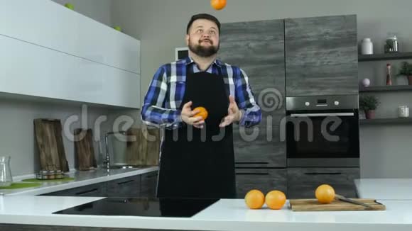 一个留着胡子的快乐胖子在现代厨房里摆弄橘子一个穿着围裙的快乐丰满的家伙把水果扔了上来慢慢视频的预览图