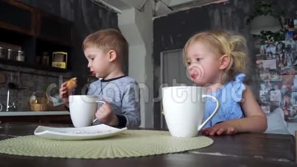 一个男孩和一个女孩在家庭厨房里喝大杯子里的茶吃牛角面包欧洲内地视频的预览图