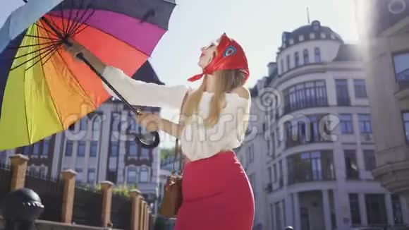 肖像年轻有趣的女人看着相机拿着五颜六色的雨伞站在街上吸引力视频的预览图