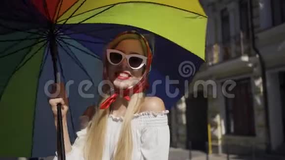可爱的年轻女子拿着五颜六色的雨伞站在街上看着镜头迷人的时尚女孩视频的预览图
