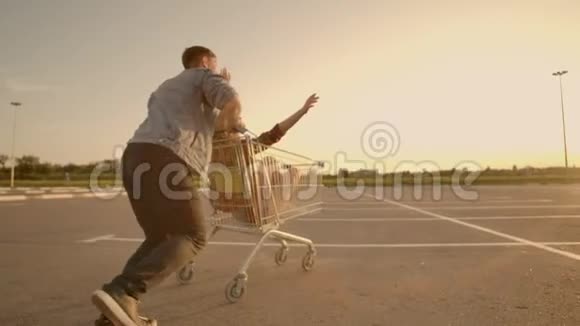 后景快乐的年轻情侣恋爱中的男人和女人在超市停车场的推车里嬉笑打闹视频的预览图