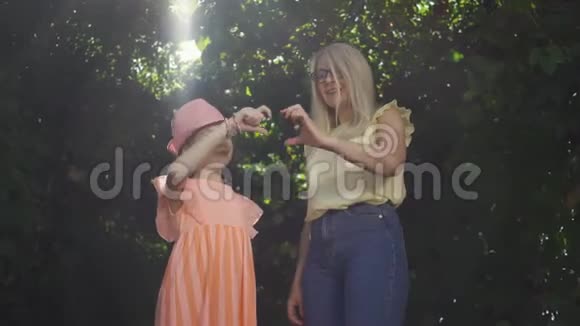 美丽的金发母亲和她的女儿在夏天的花园或公园里用手指做心形幸福家庭视频的预览图