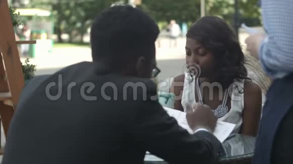 非裔美国人和他的女伴坐在外面的咖啡馆里点餐视频的预览图