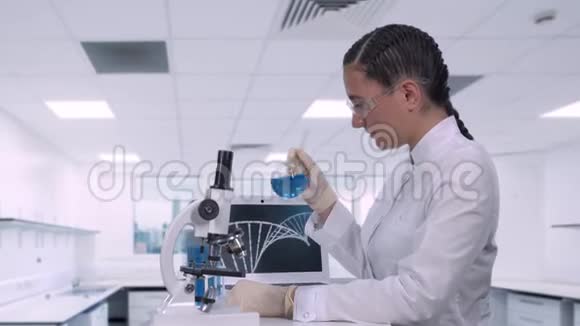 一位女实验室技术人员坐在现代医学实验室的笔记本电脑旁的桌子旁检查一个蓝色的样本视频的预览图