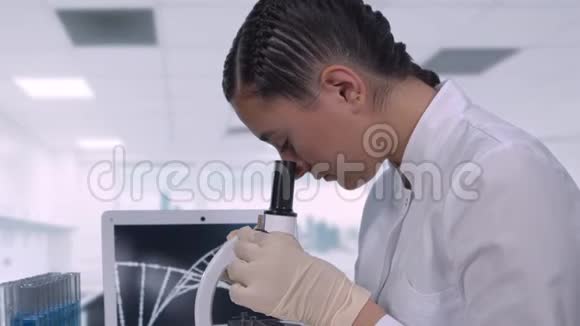 一位女实验室技术人员坐在现代医学实验室的笔记本电脑旁的桌子旁看生物样本视频的预览图