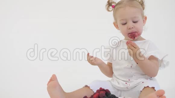 可爱的宝宝在浅色背景下吃多汁的覆盆子和黑莓视频的预览图