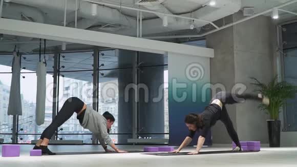 两个漂亮的女人在瑜伽练习室里同时向后退狗嘴朝下腿抬高视频的预览图