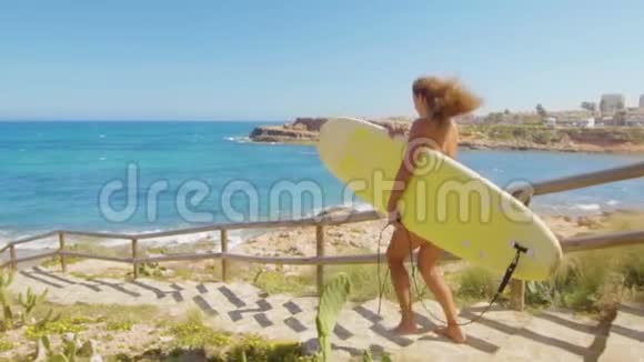 皮肤黝黑的性感女孩带着冲浪板在沙滩上散步穿着比基尼泳装的漂亮年轻女子概念视频的预览图