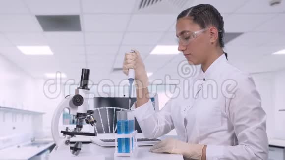 一位女实验室技术人员坐在桌子旁用微型吸管将蓝色液体样品转移到不同的管子上视频的预览图