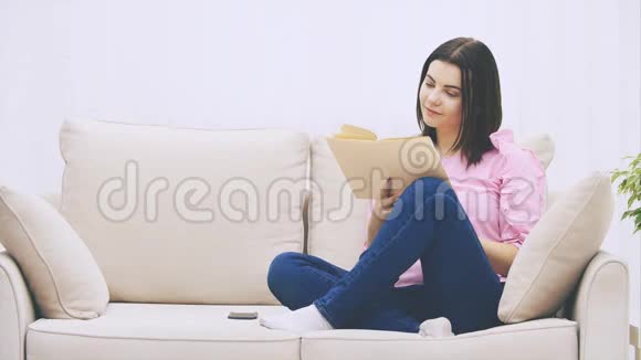 敏锐的年轻女性正坐在沙发上以洛托斯的姿势看书对情节做出情感反应视频的预览图